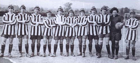L'équipe des Dick Kerr Ladies posant pour la photo, dans leurs tenues de matchs (maillots rayés, shorts, chaussettes longues, chapeaux), alignées et les bras croisés.